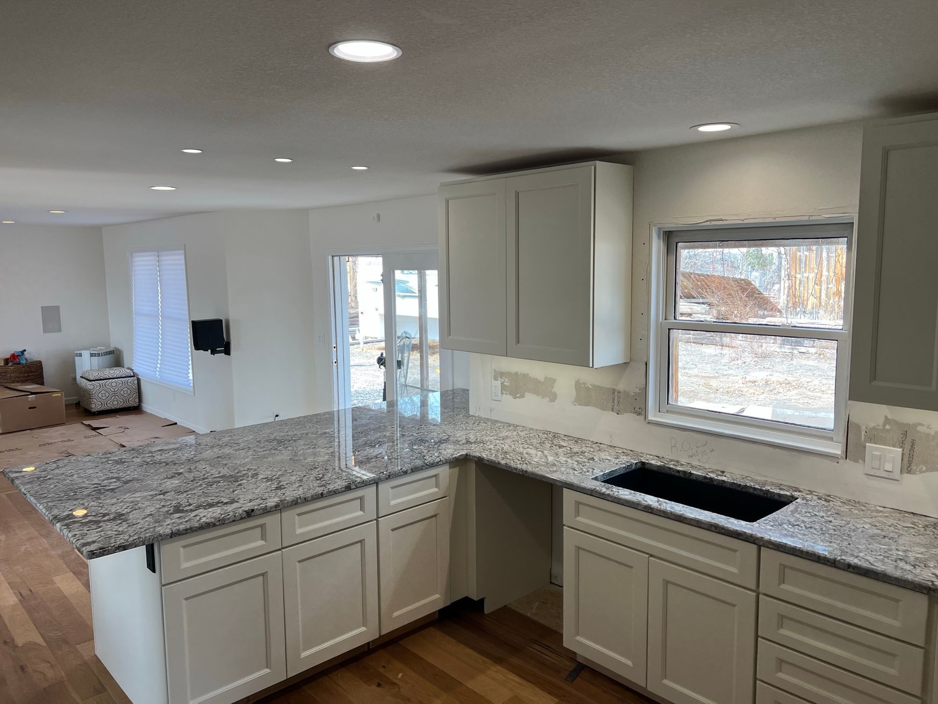 Bright kitchen with white cabinets, granite counters, and a window over the sink under renovation.