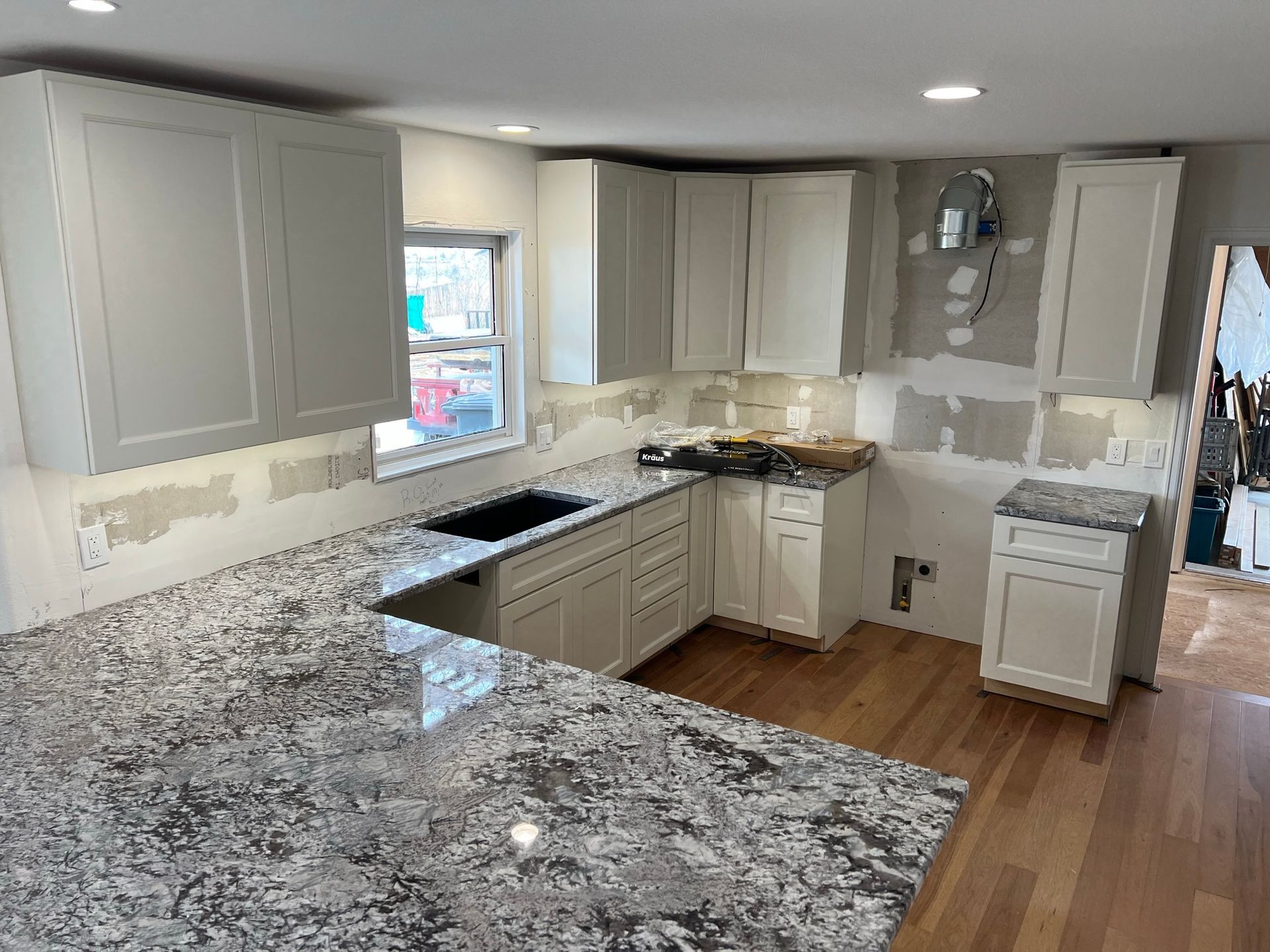 Partially renovated kitchen with white cabinets, granite countertops, and wood flooring