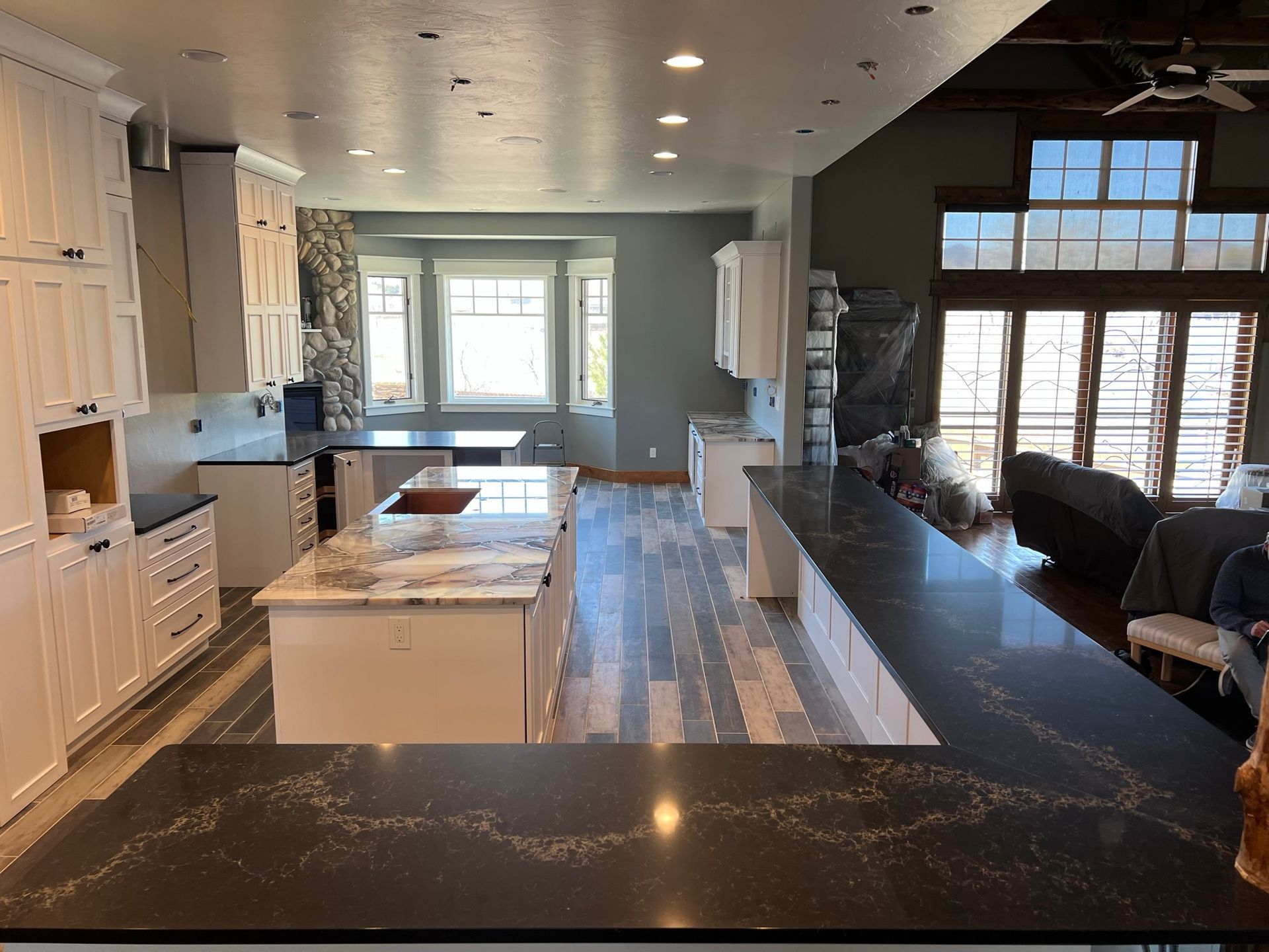 Modern kitchen with white cabinets, black countertops, island, and large windows overlooking a living area