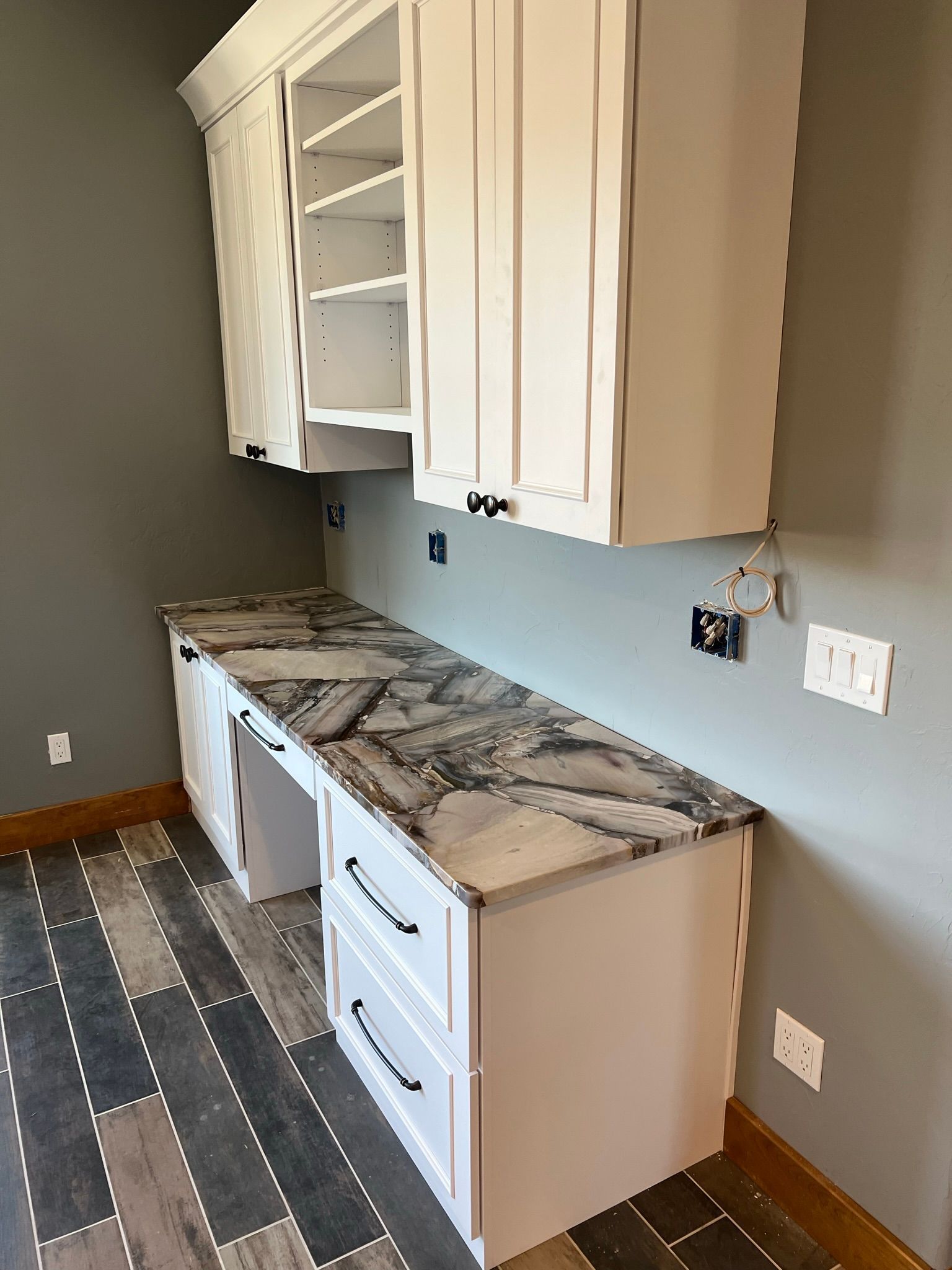 Empty kitchen with white cabinets, marble-look countertop, and gray walls under construction