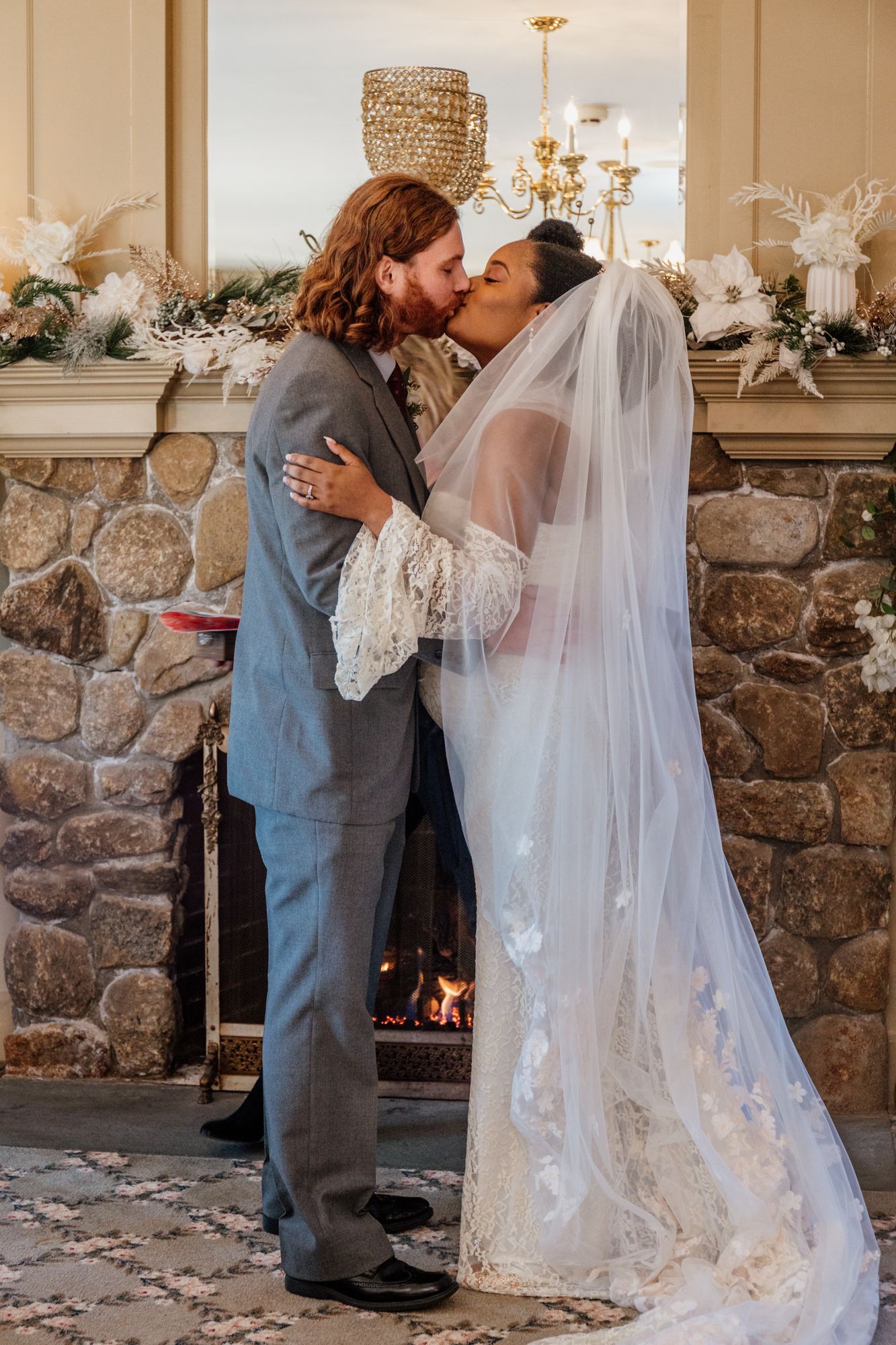 A bride and groom are kissing in front of a fireplace.