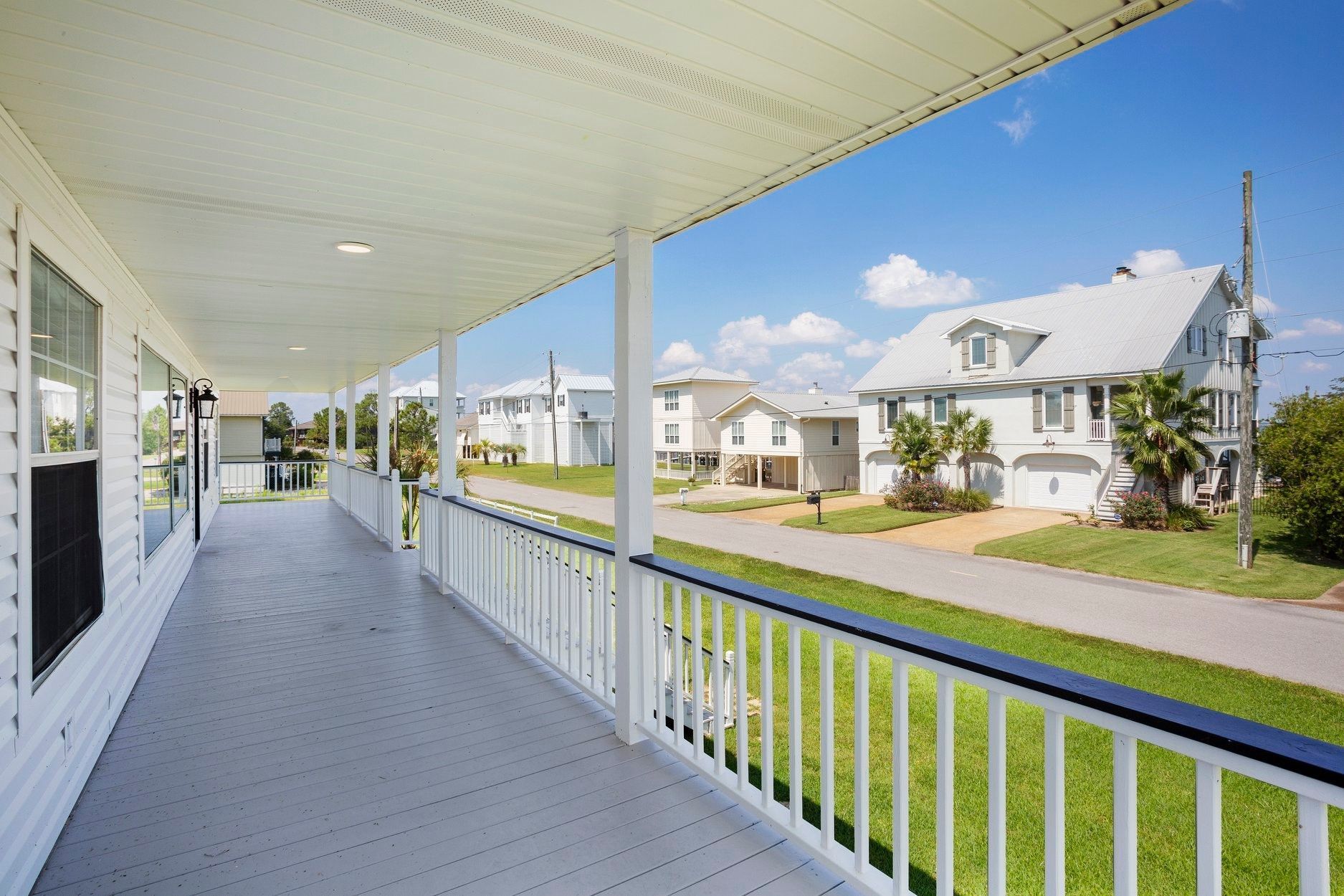 White porch with a railing overlooking a street lined with white houses on a sunny day.