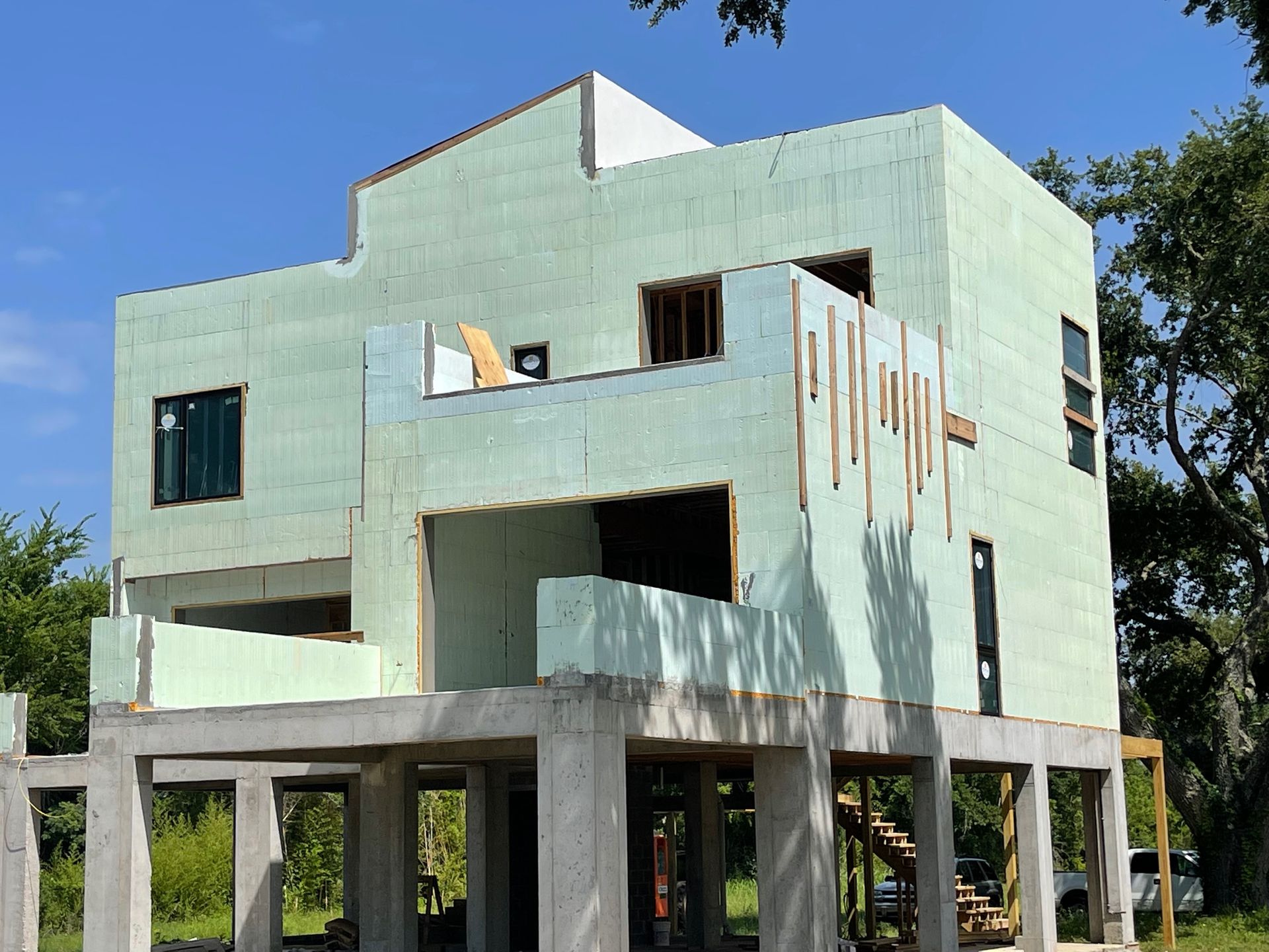Two-story house under construction with light green insulated concrete forms on a concrete pier foundation, blue sky.