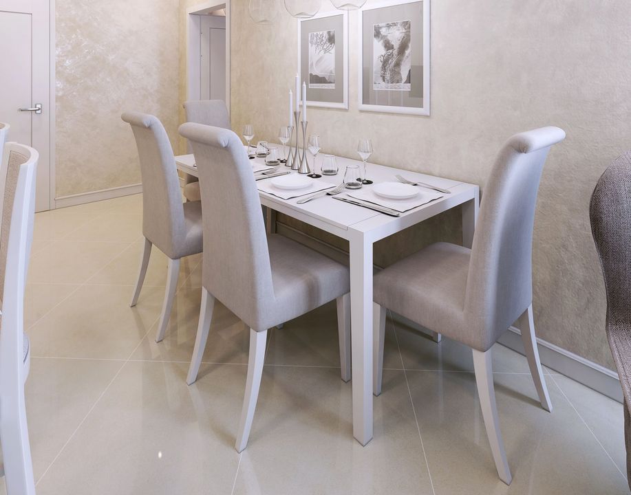 Sala da pranzo moderna con tavolo bianco e quattro sedie imbottite accanto a una parete piastrellata.