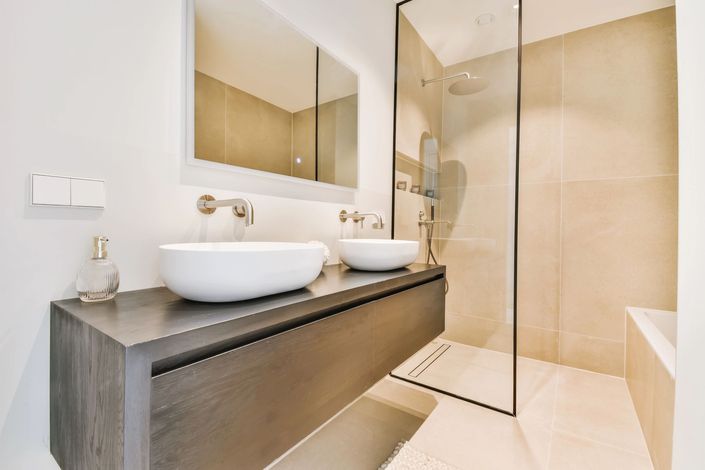 Bagno moderno color beige con doppio lavabo a ciotola, specchio a parete e box doccia in vetro.