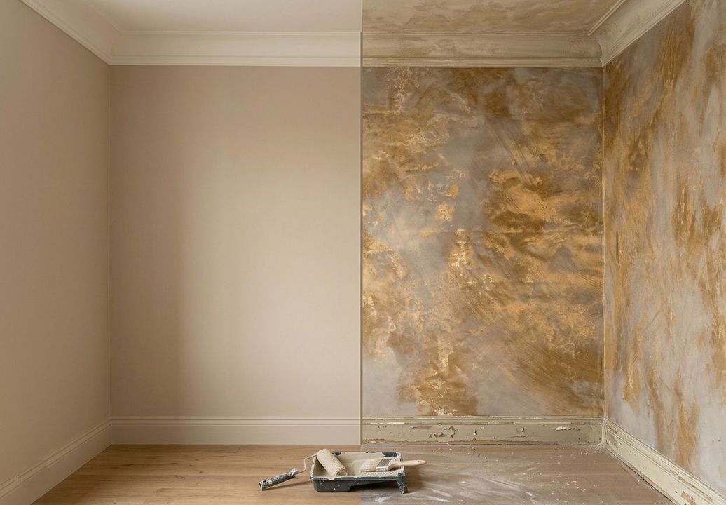 Stanza vuota con pareti beige e una parete decorativa dorata in fase di ristrutturazione, attrezzi sul pavimento.