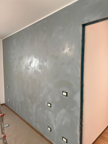 Parete interna grigia appena dipinta con diverse prese elettriche e un'apertura per una porta sulla destra.