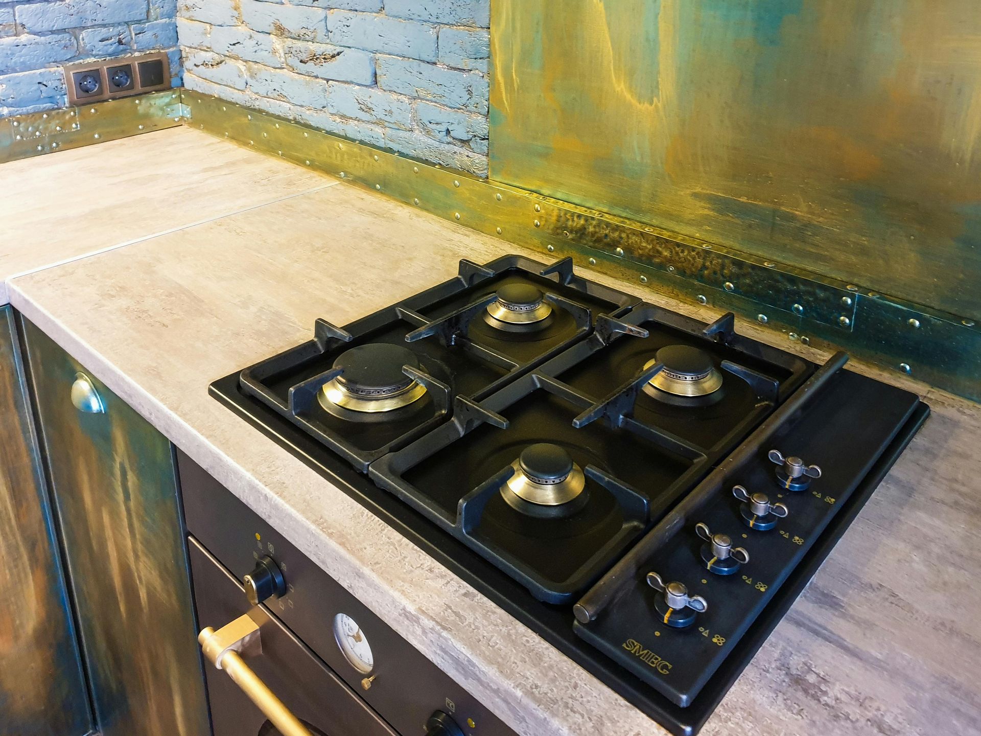 Kitchen countertop with a black gas cooktop and beige counter against a blue brick backsplash.