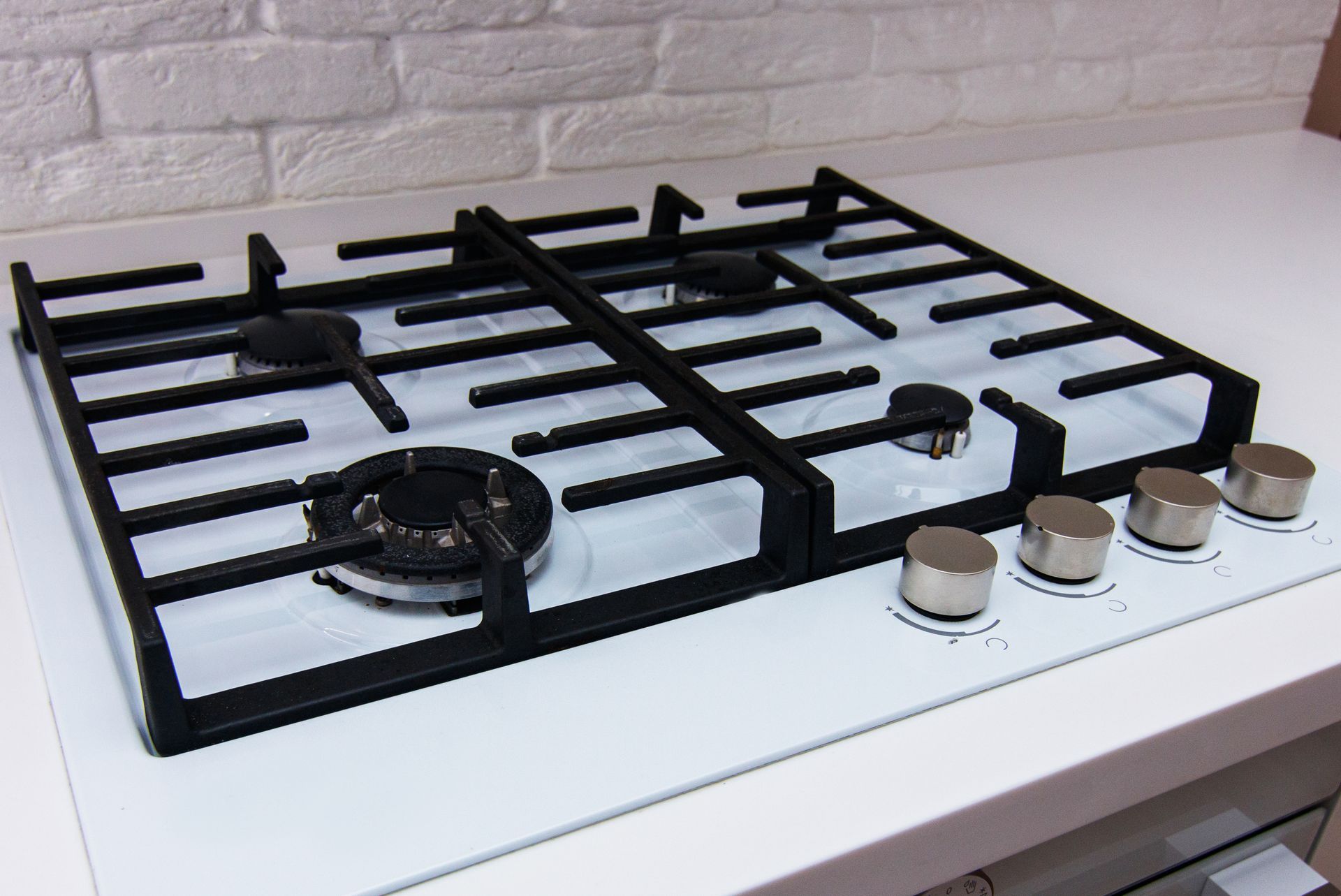 White gas cooktop with four burners and silver control knobs on a kitchen counter