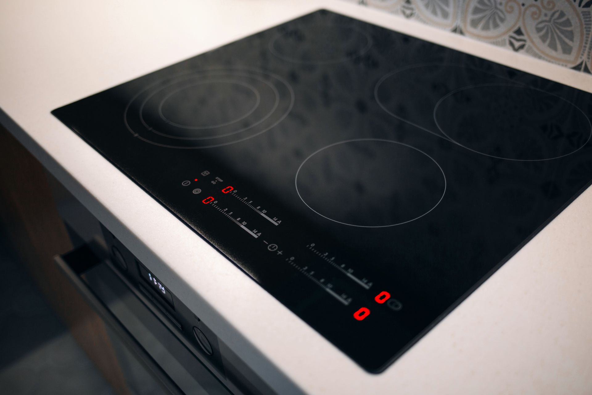 Black glass electric cooktop with four burners and red control lights on a white countertop