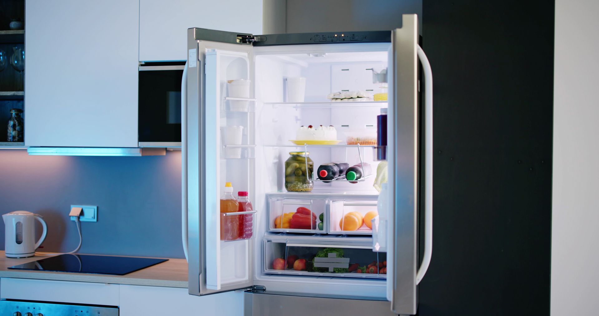 Open refrigerator in a modern kitchen, showing shelves with fruits, vegetables, and condiments.