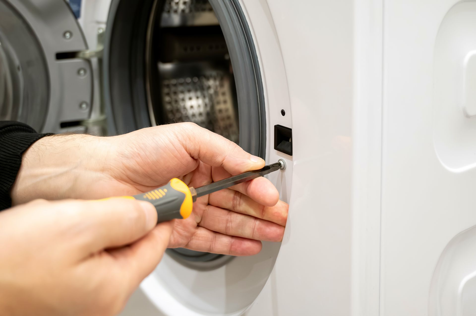 Hand tightening a screwdriver on a washing machine door latch area