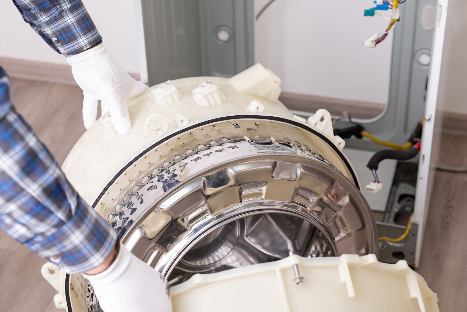 Gloved worker handling a large industrial machine with a metal drum and white casing in a workshop