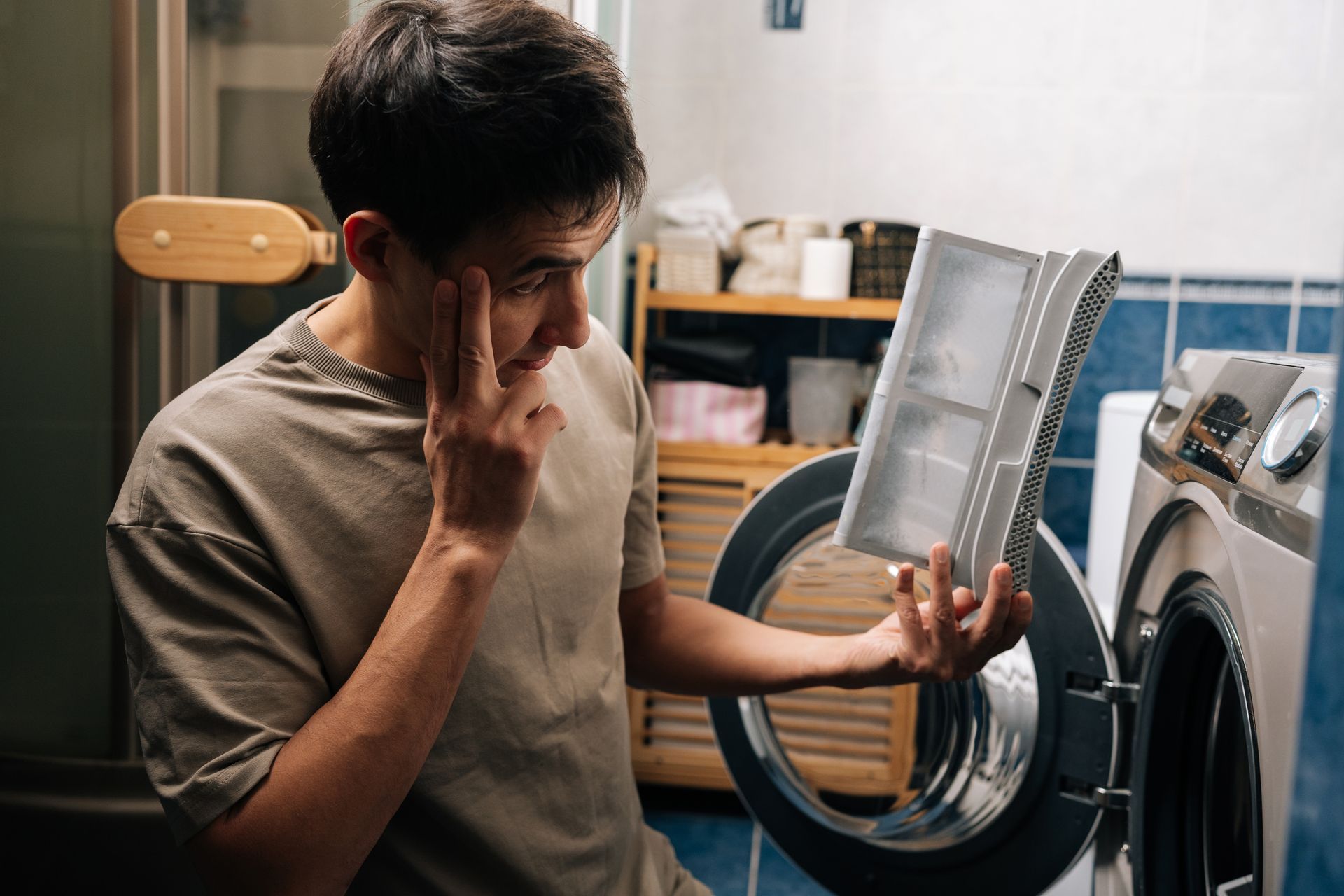 Frustrated person inspecting a washing machine with the door open in a laundry room