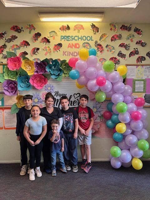 A group of children are standing in front of a wall decorated with balloons and flowers.