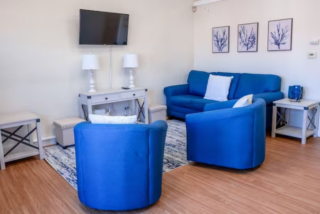 A living room with a blue couch , blue chairs , and a flat screen tv.