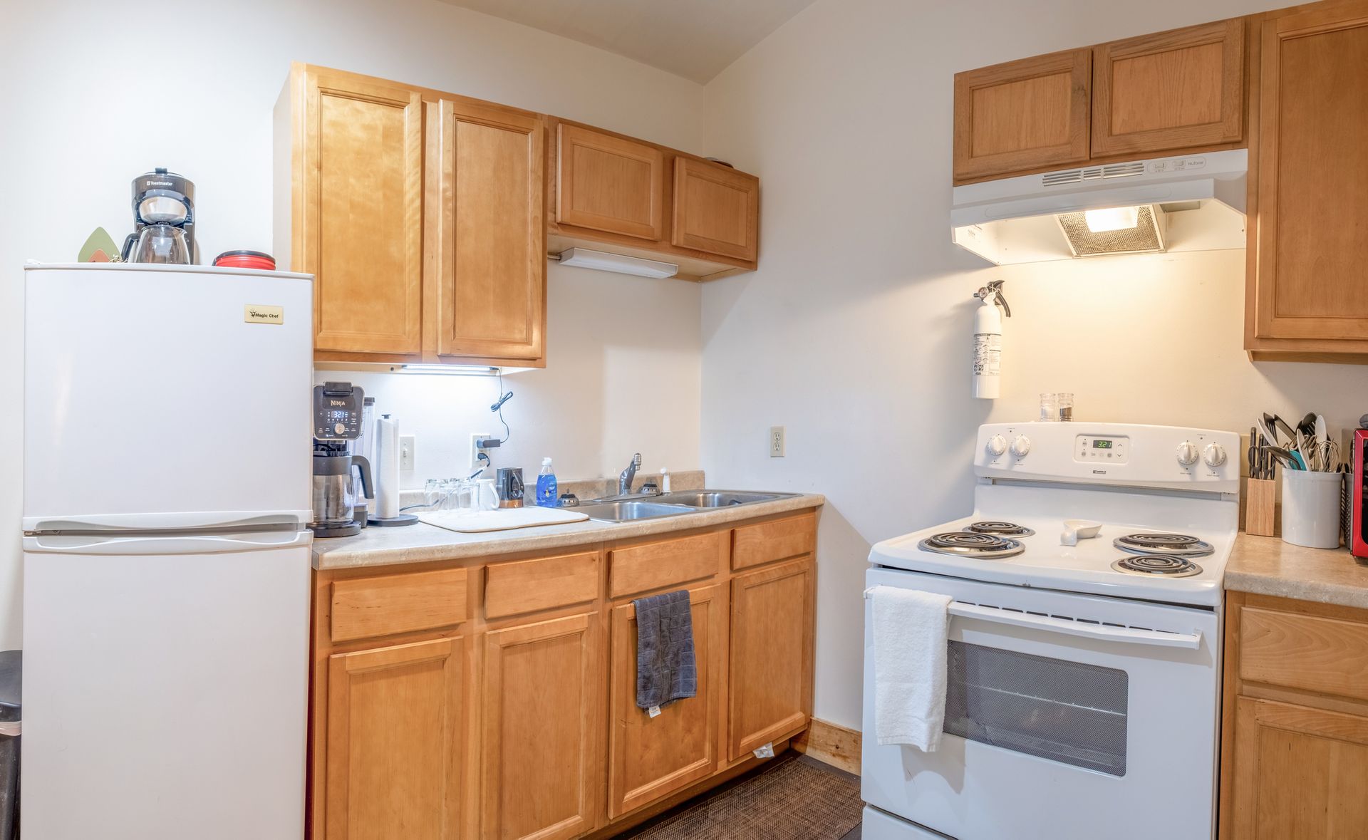 A kitchen with wooden cabinets , a white refrigerator , a stove , and a sink.
