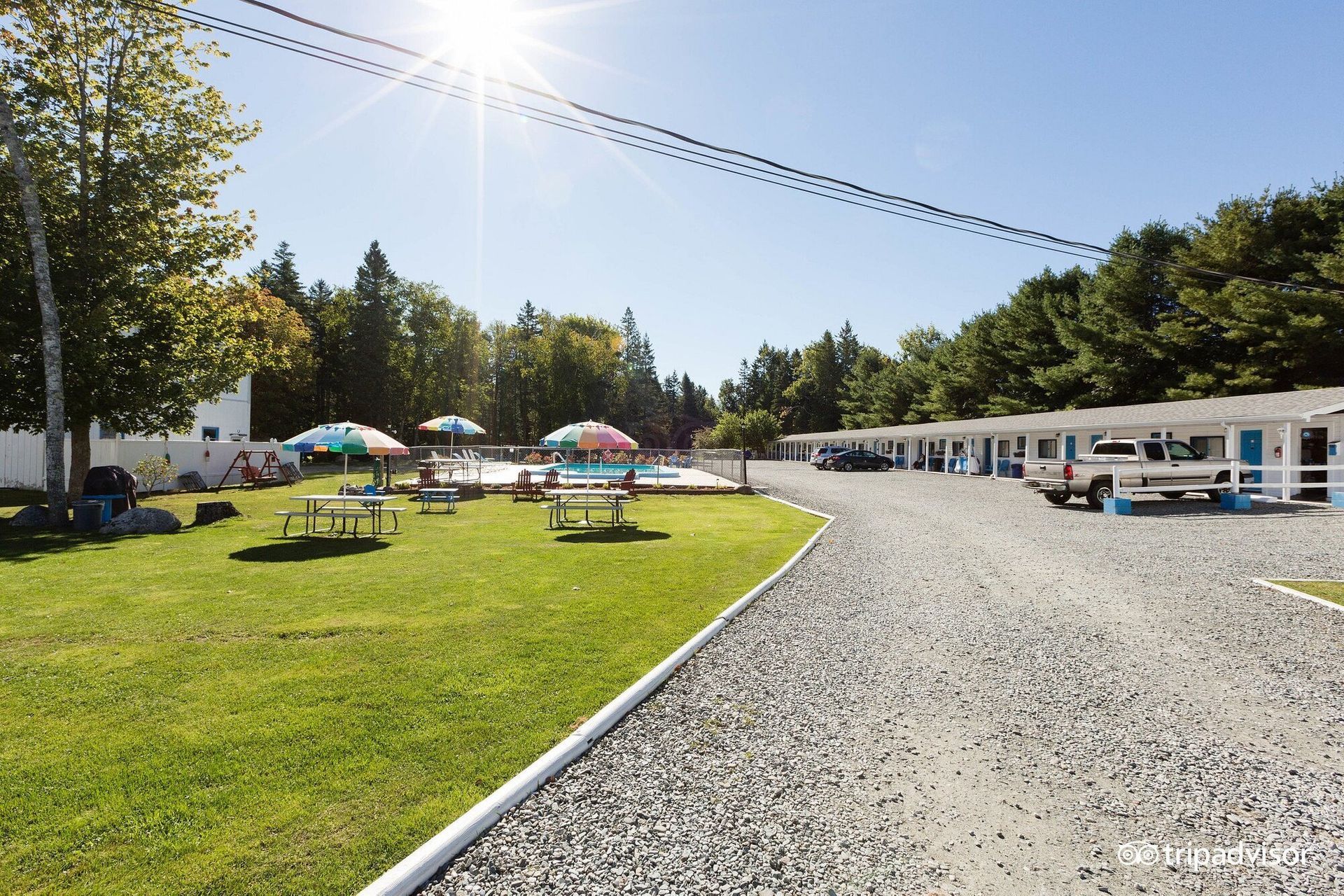 A gravel road leading to a motel with umbrellas and picnic tables