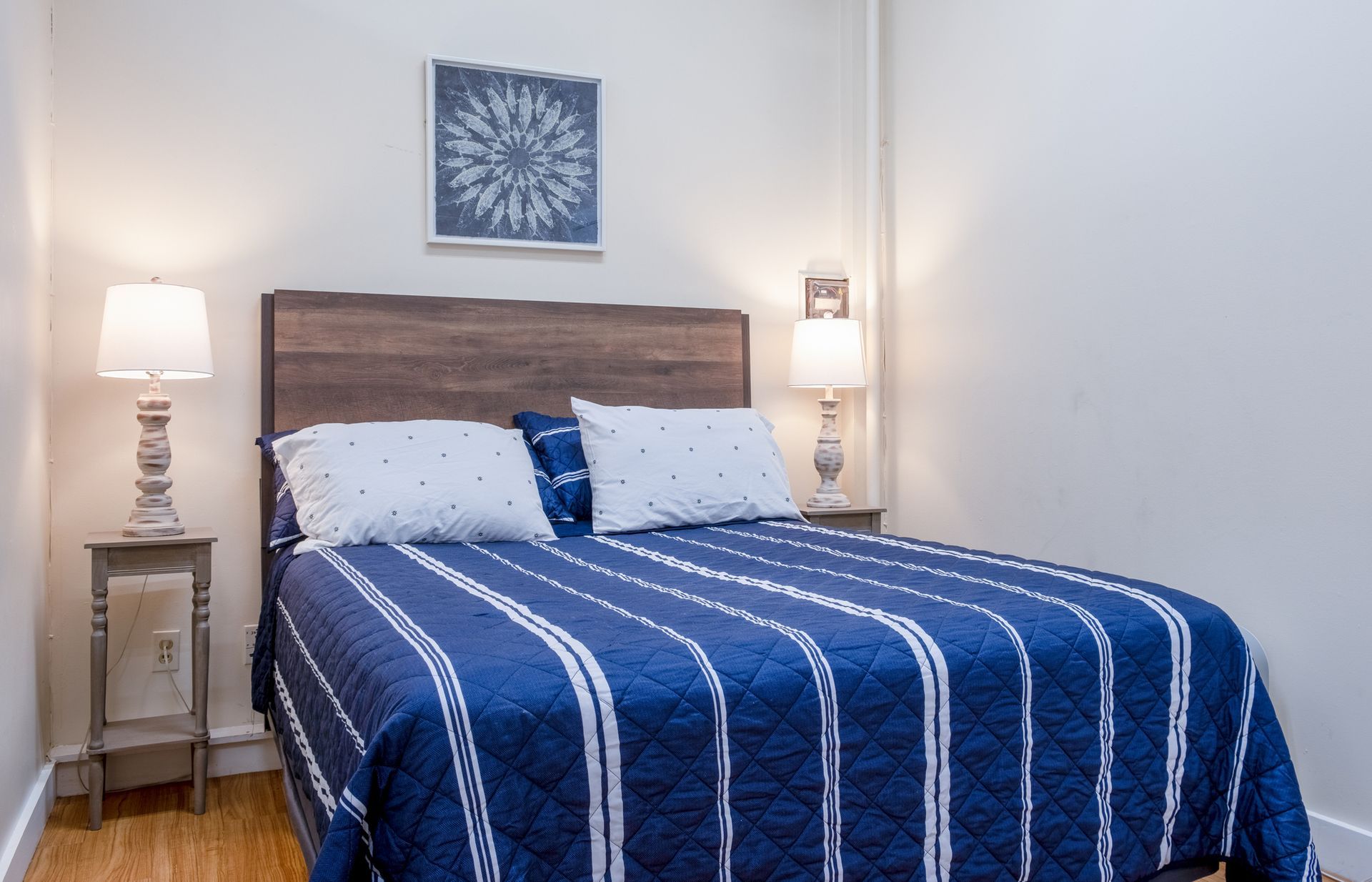 A bedroom with a bed , nightstand , lamp and a picture on the wall.