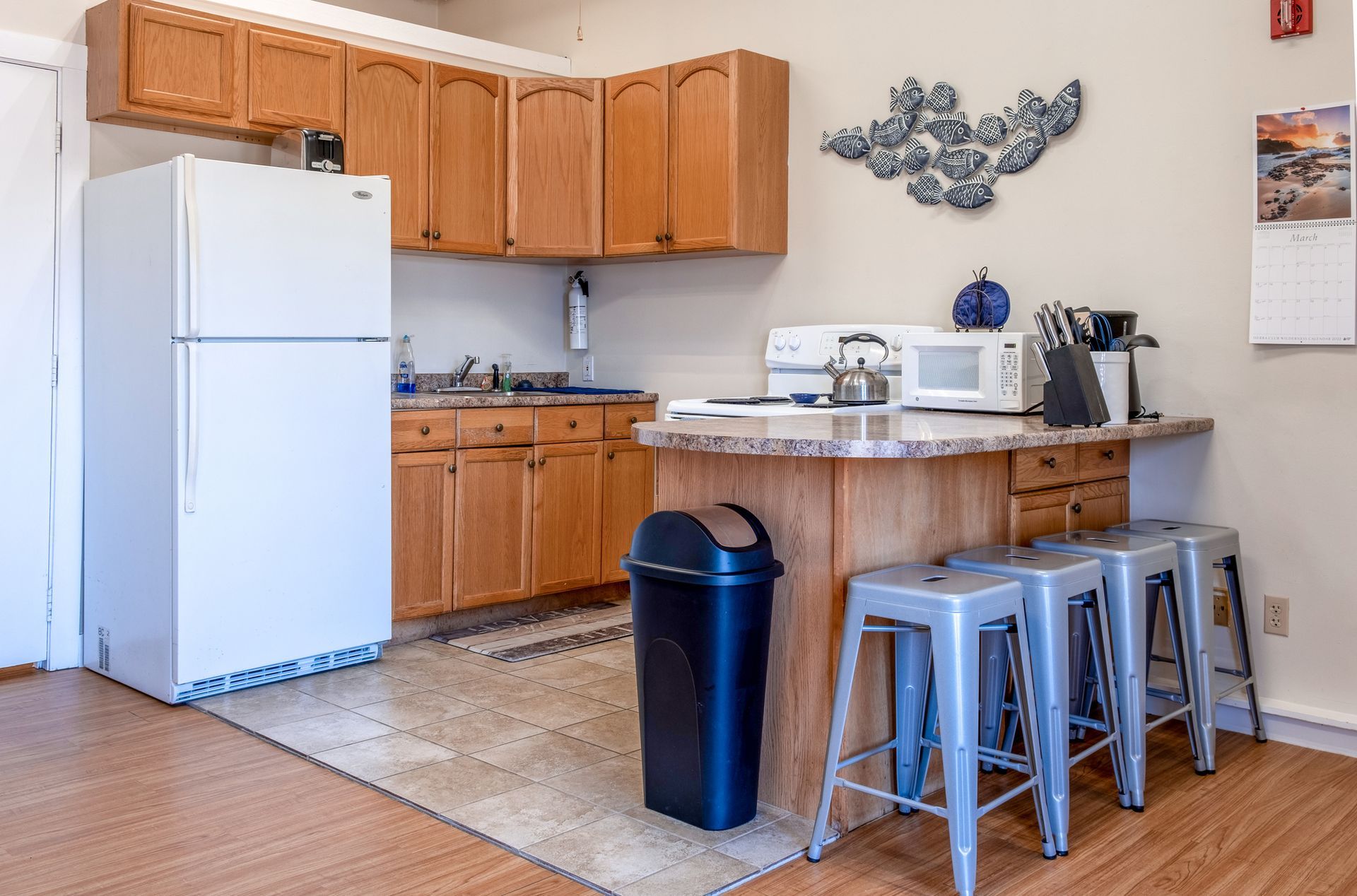 A kitchen with a refrigerator , microwave , sink , and stools.