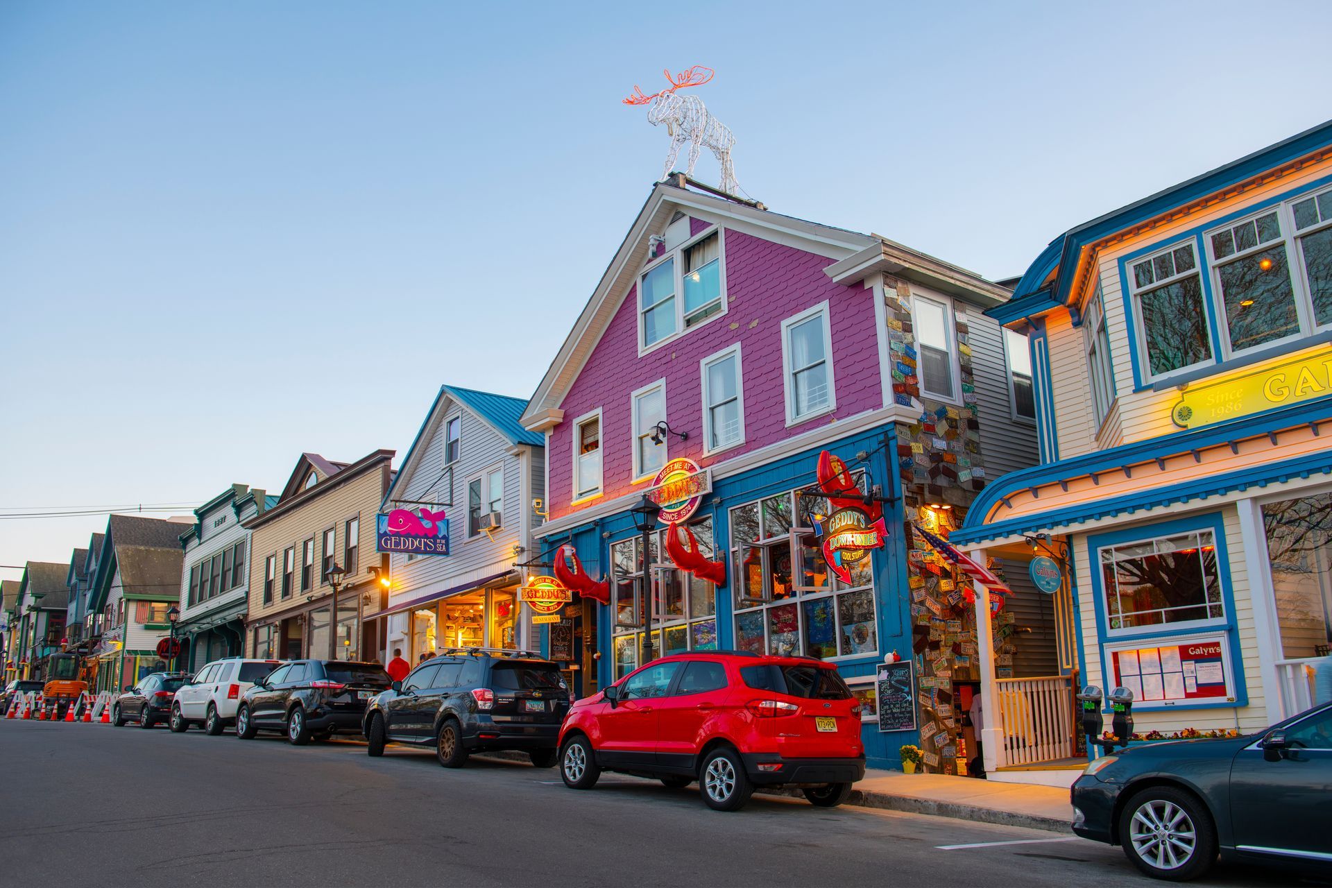 A red car is parked in front of a row of colorful buildings.