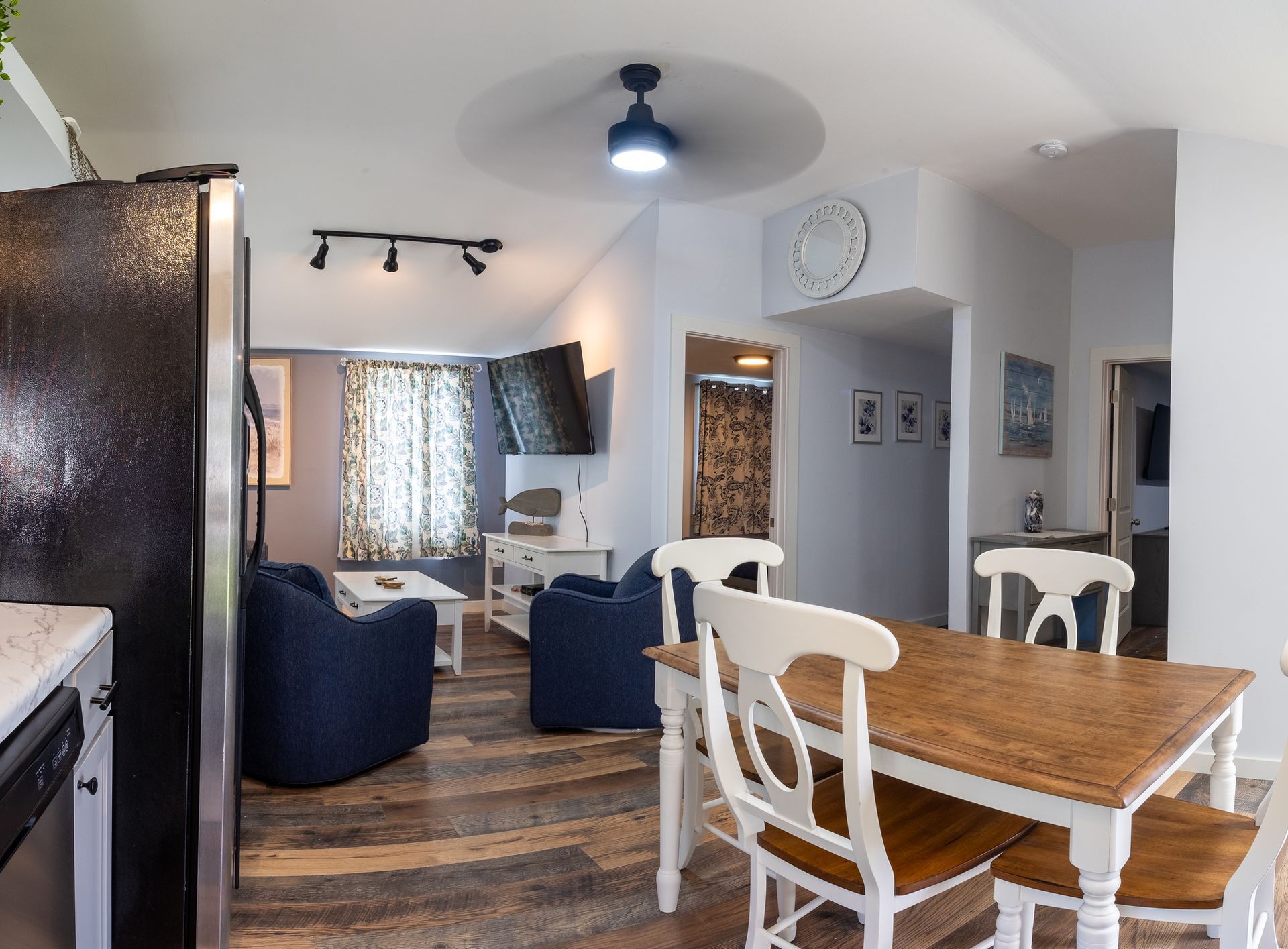 A living room with a table and chairs and a black refrigerator.