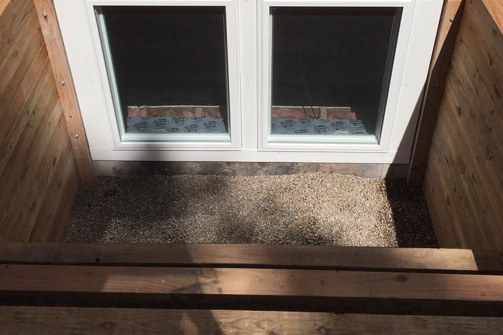 A window in a basement with a wooden staircase leading up to it.