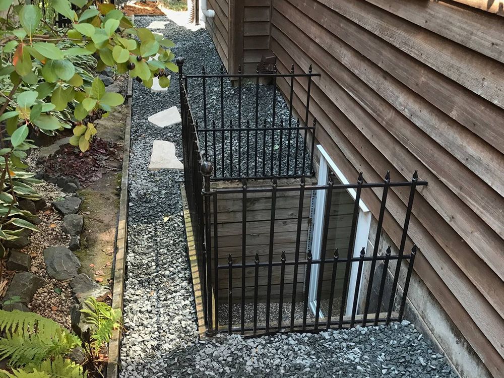 A fence surrounds a window in the basement of a house