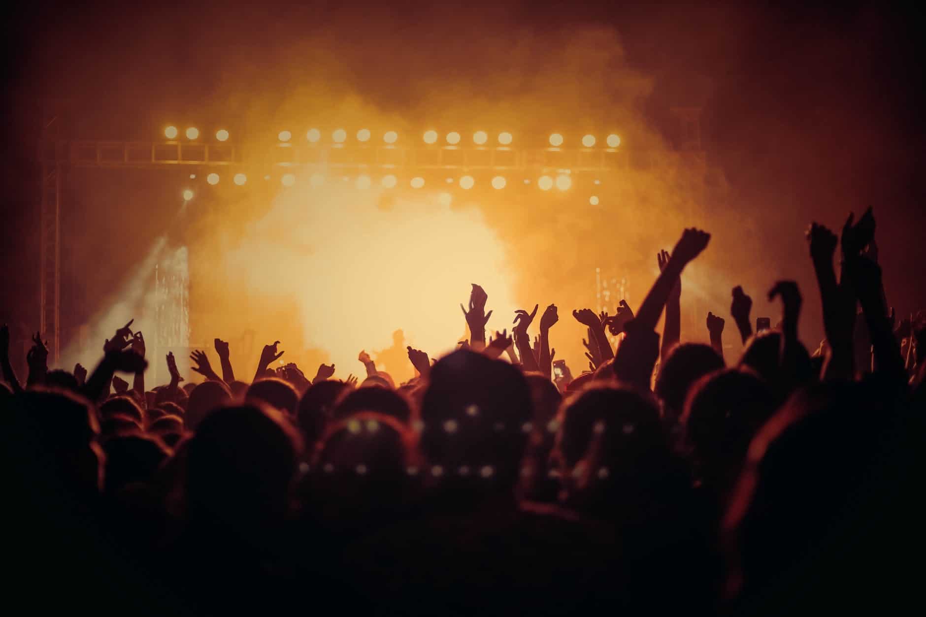 Une foule de gens se tient devant une scène lors d'un concert.