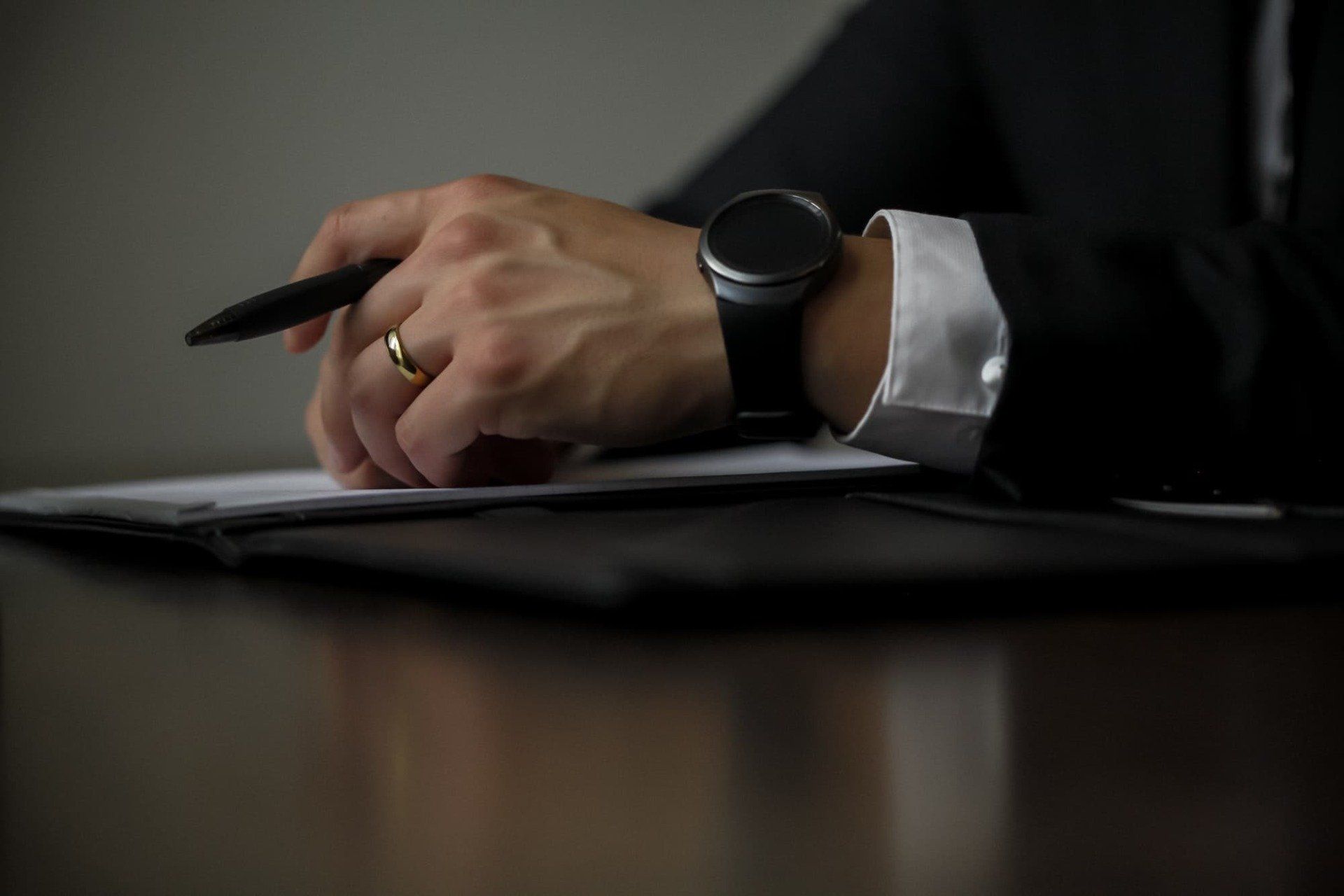 Un homme est assis à une table et écrit sur un morceau de papier avec un stylo.