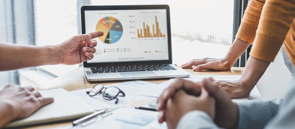 Des personnes consultent des graphiques de données commerciales sur l'écran d'un ordinateur portable lors d'une réunion de travail collaborative.