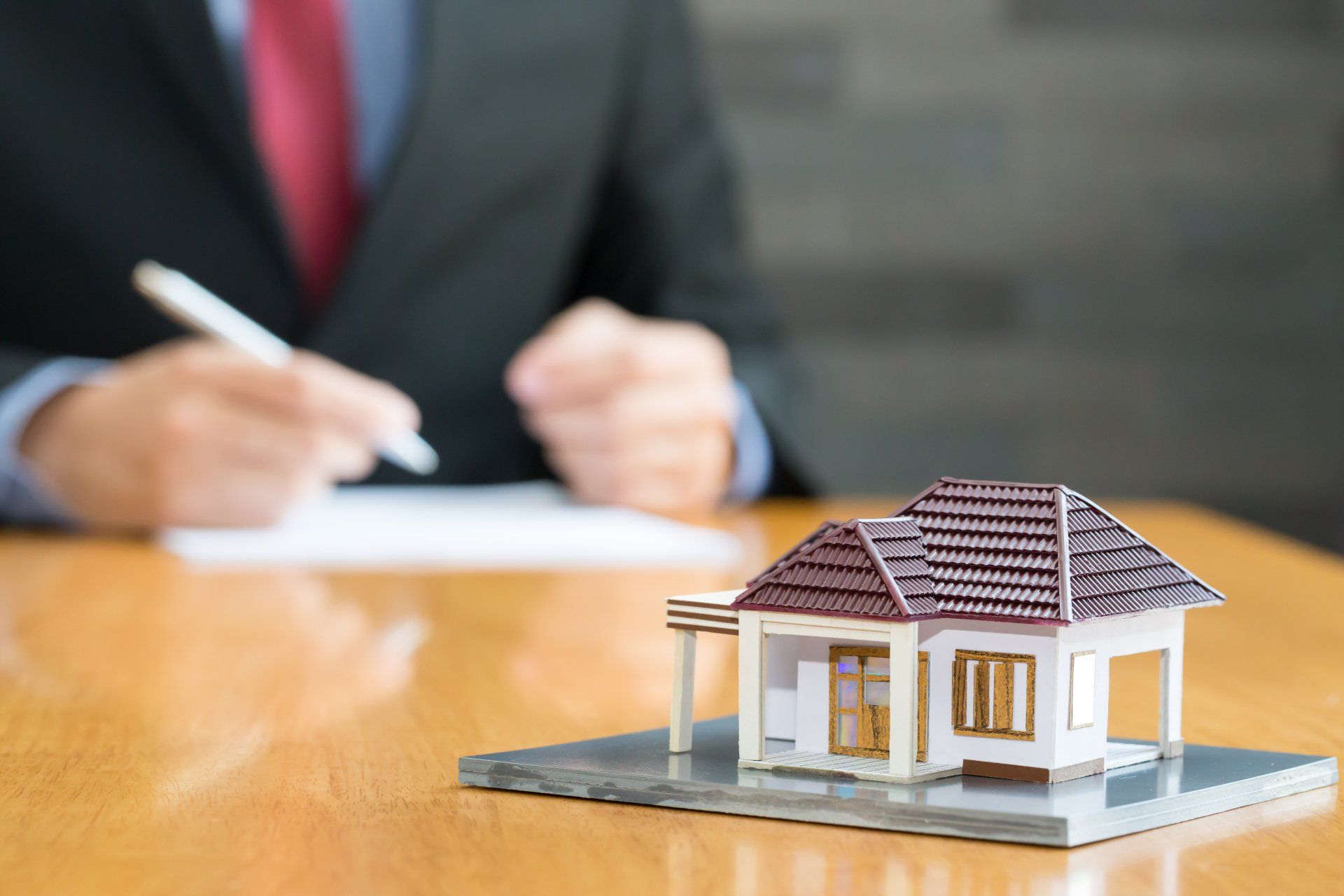 Un homme signe un document à côté d'une maison modèle sur une table.