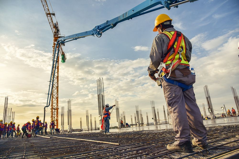 Un ouvrier du bâtiment se tient devant une grue sur un chantier de construction.