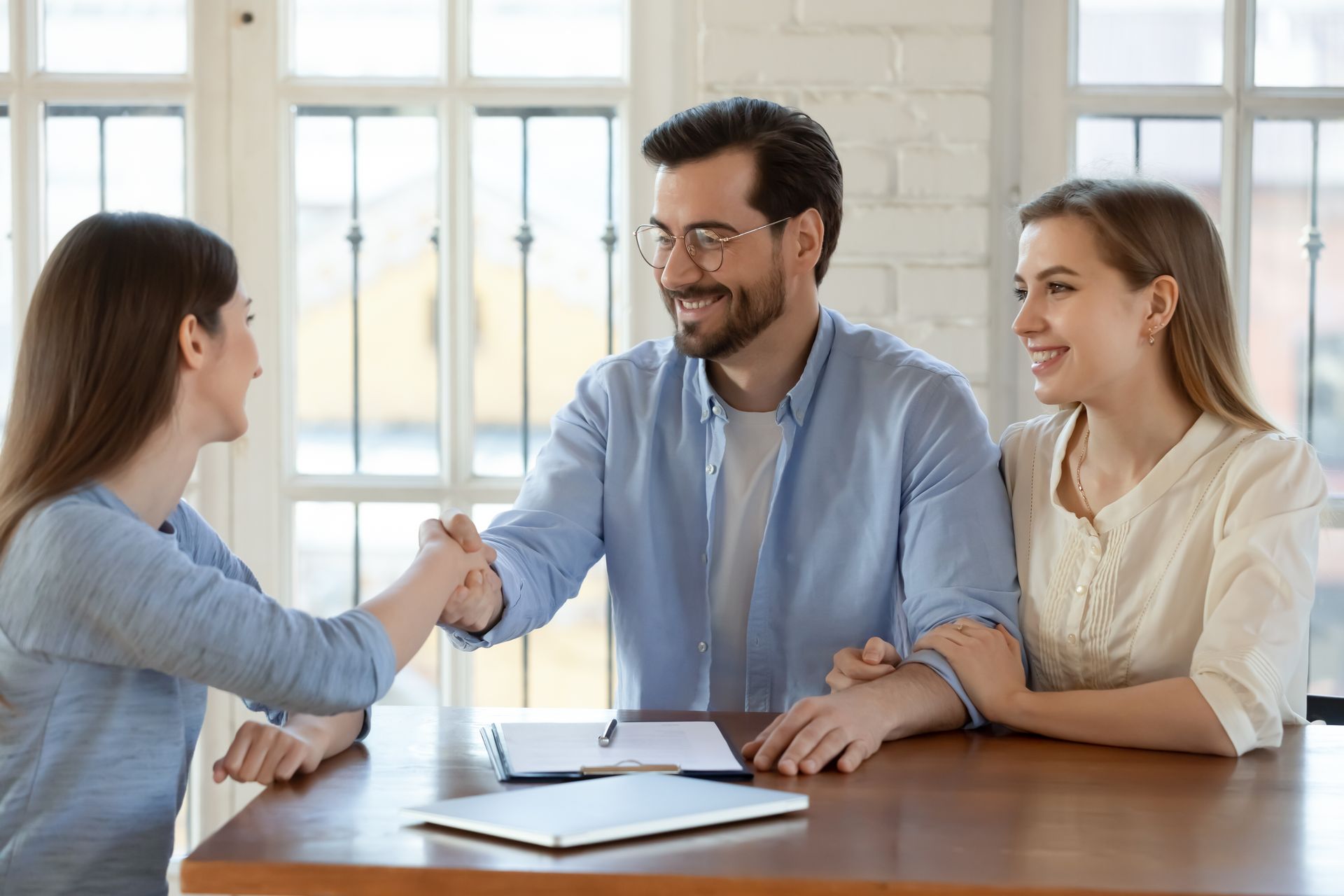Trois personnes se rencontrent autour d'une table et se serrent la main dans un bureau lumineux.