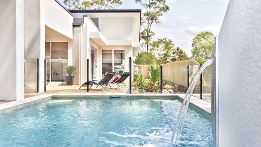 A swimming pool with a waterfall in front of a house.