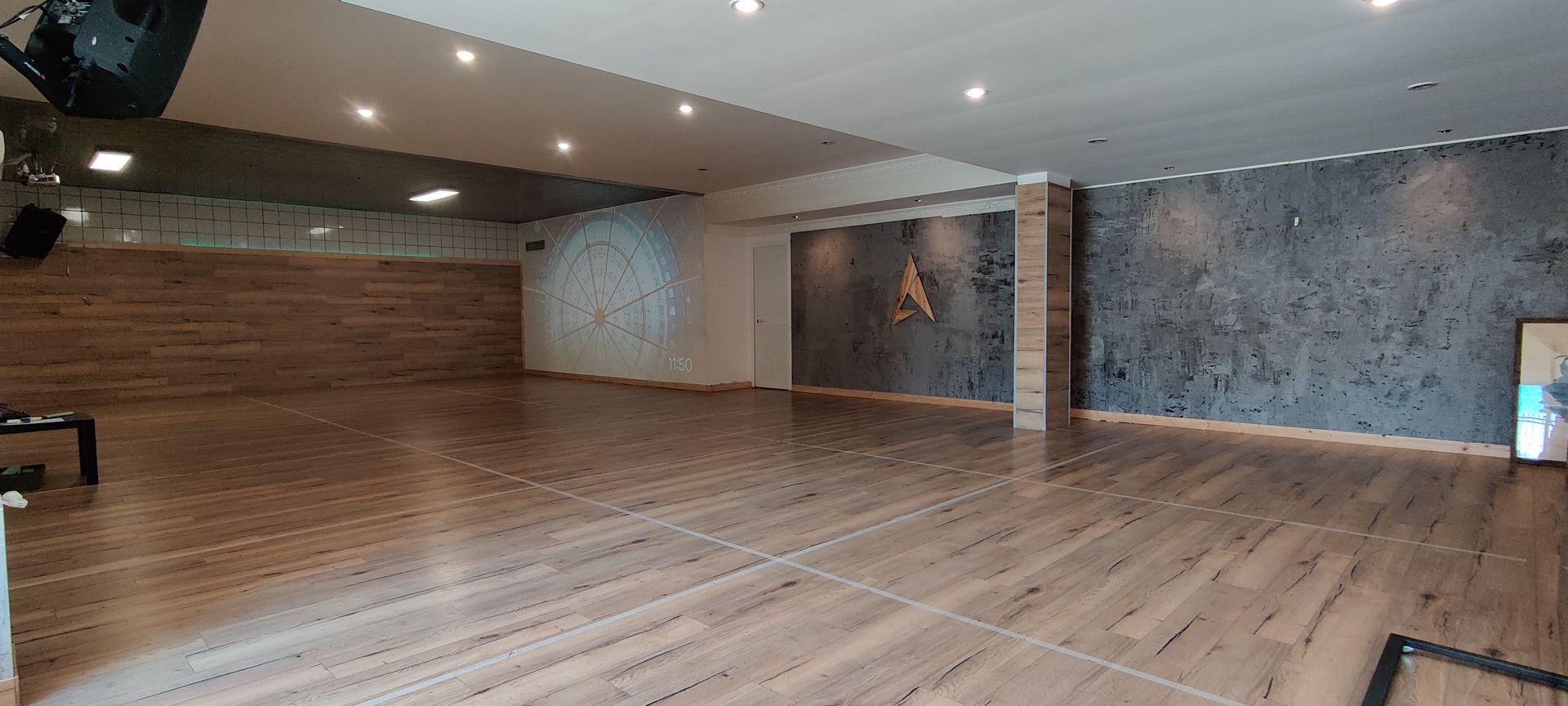 Studio di danza vuoto con pavimento in legno e pareti decorative, con un logo sulla parete centrale.