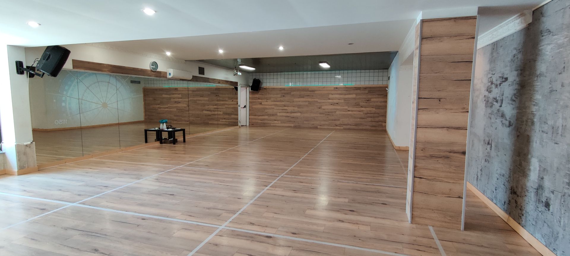 Studio di danza vuoto con pavimenti in legno, specchi e pareti in legno. Altoparlanti montati sul soffitto.