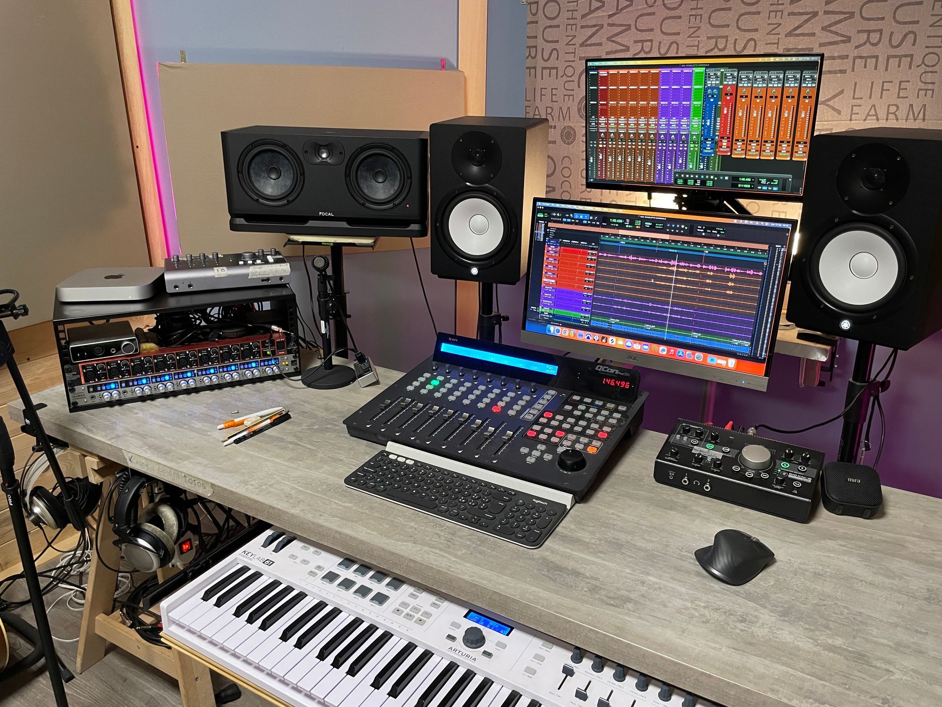 Uno studio di produzione musicale con più schermi, altoparlanti e una tastiera su una scrivania.