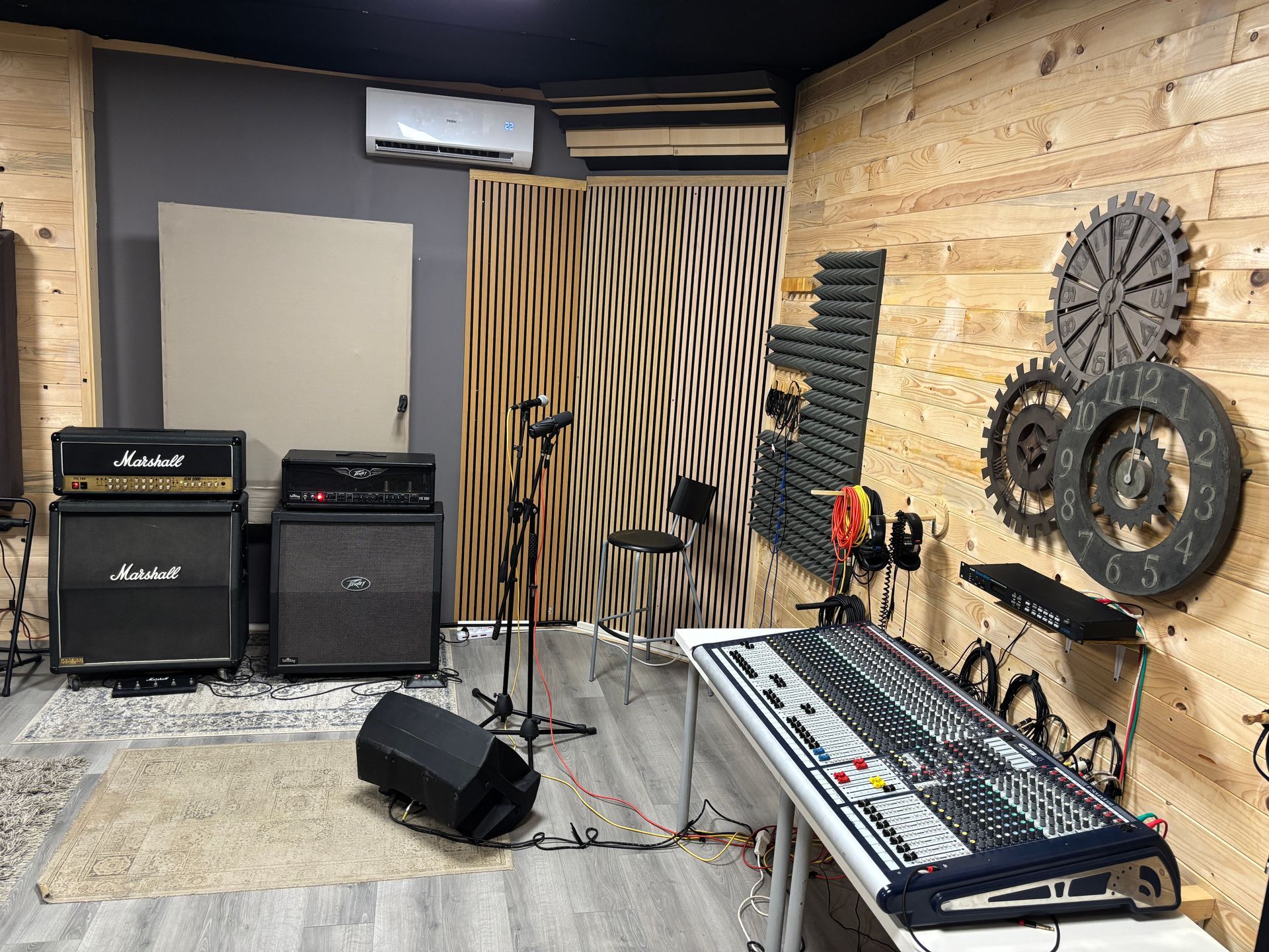 Studio di registrazione con amplificatori, console di missaggio, microfoni e insonorizzazione, con dettagli in legno e grigio.