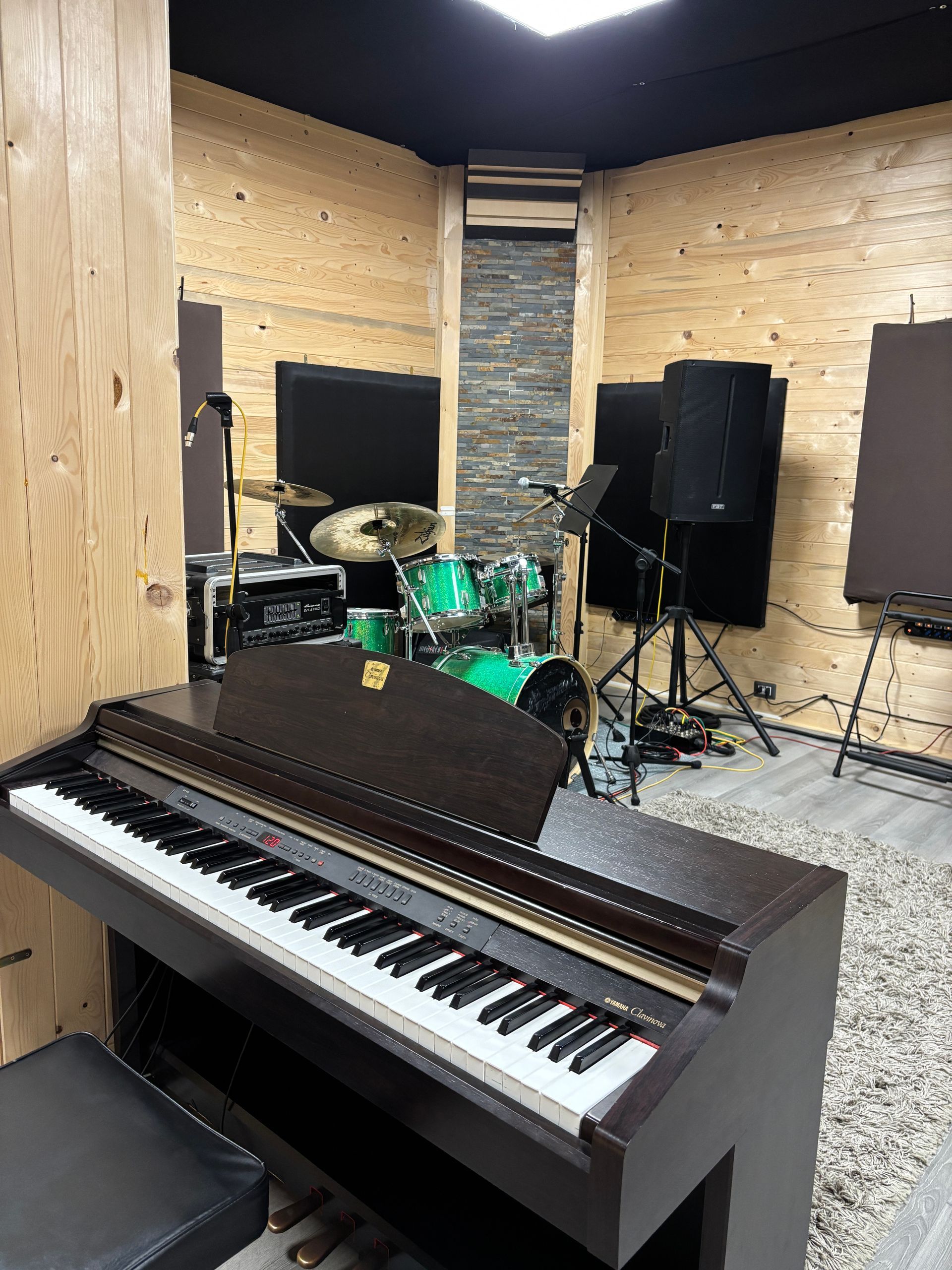 Pianoforte e batteria in uno studio musicale, con altoparlanti e pannelli insonorizzati.