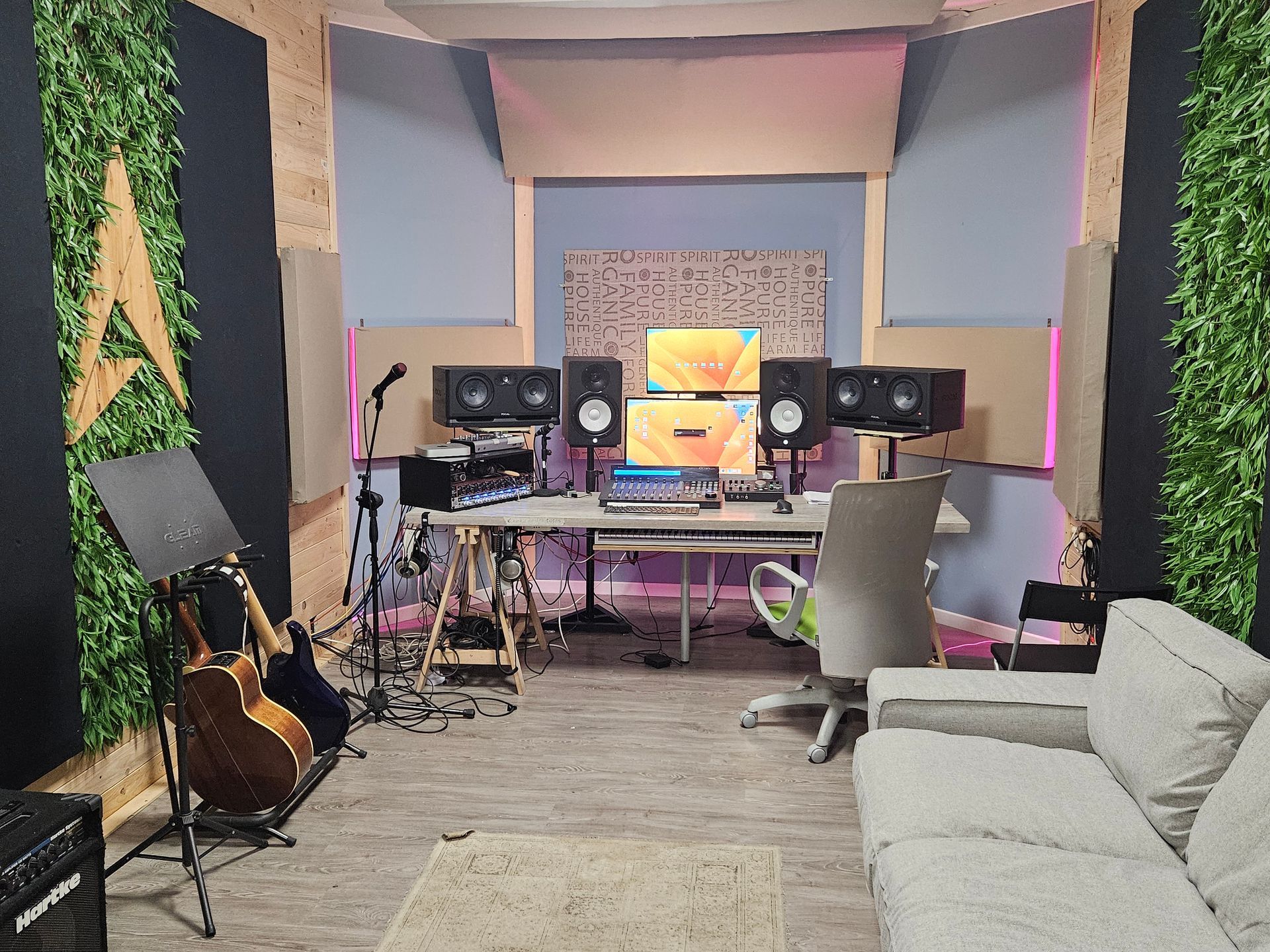 Studio musicale con scrivania, monitor, altoparlanti, microfono, strumenti e divano. Dettagli in verde e legno.