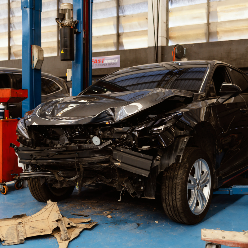 Black car with severe front-end damage in an auto repair shop on a lift.