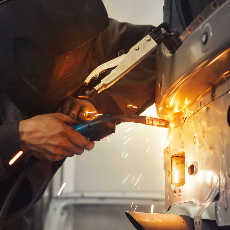 Welder using a torch on a metal vehicle panel, with bright sparks flying in a workshop