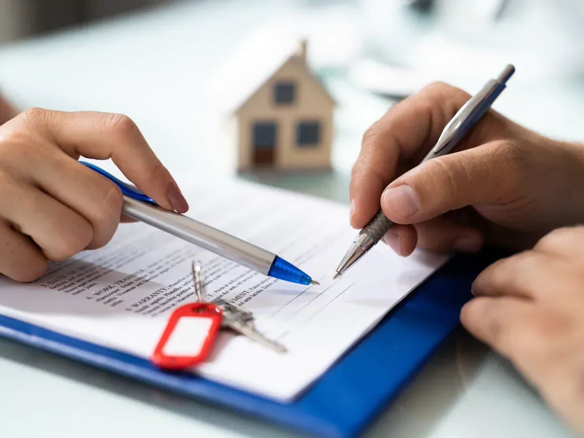 A person discussing property management services with two pens about to sign a contract. 