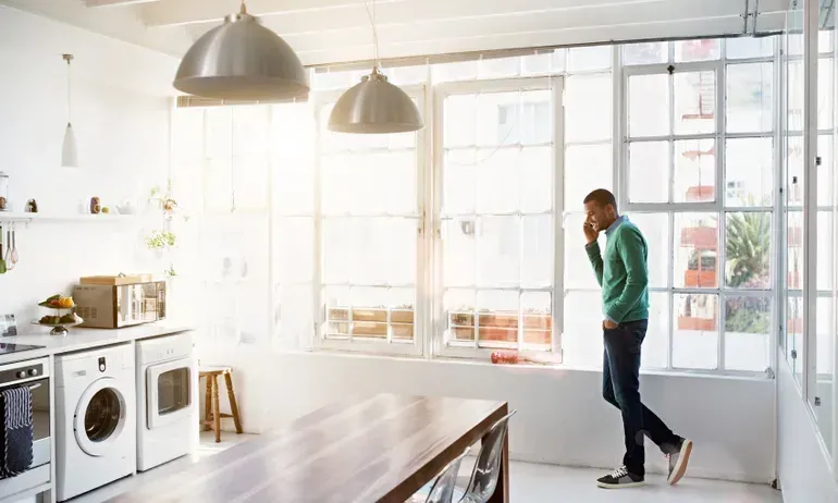 A man is standing in a kitchen talking on a cell phone. A man is standing in a kitchen talking on a cell phone.
