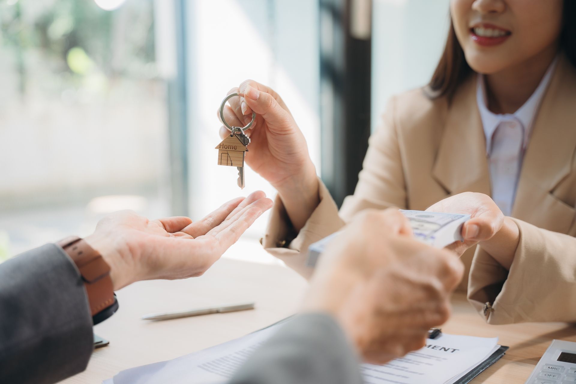 Woman handing keys with house charm to person, likely a real estate transaction. Woman handing keys with house charm to person, likely a real estate transaction.