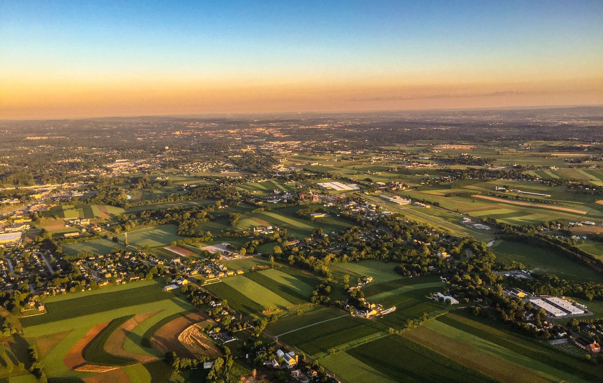 An aerial view of a city surrounded by fields and trees at sunset.