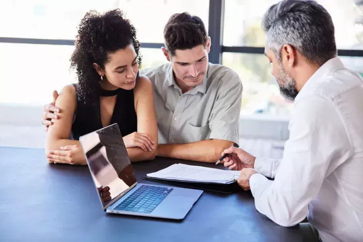 A man and a woman are sitting at a table looking at a laptop. A man and a woman are sitting at a table looking at a laptop.
