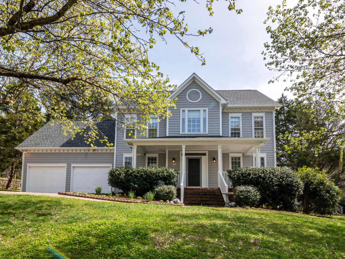 Two-story gray house with white trim, two-car garage, and front porch; green lawn and trees.
