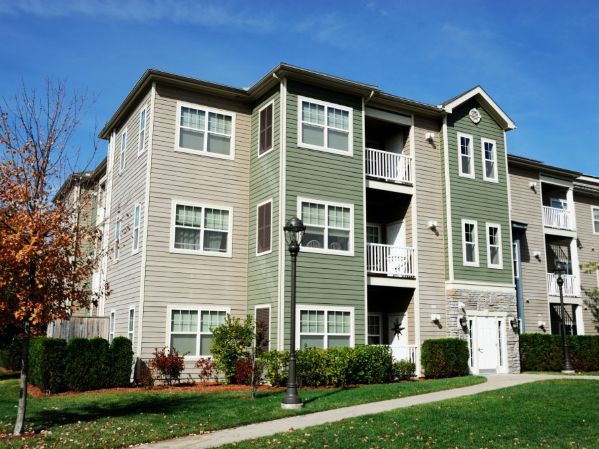 A large apartment building with a lot of windows and a sidewalk in front of it.